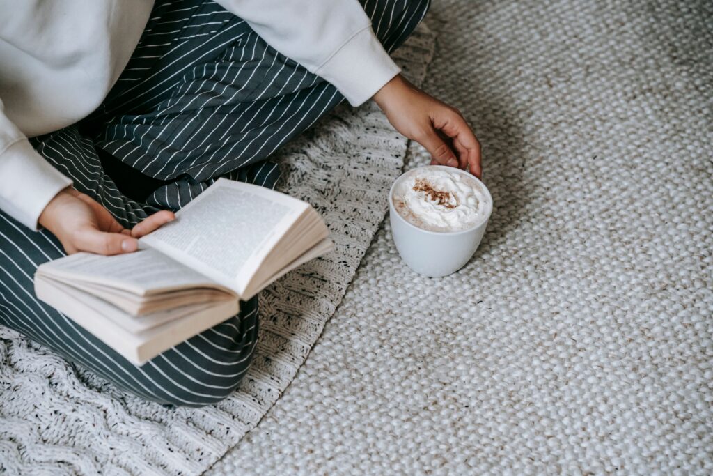 Persona leyendo un libro en el suelo junto a una taza de café con crema